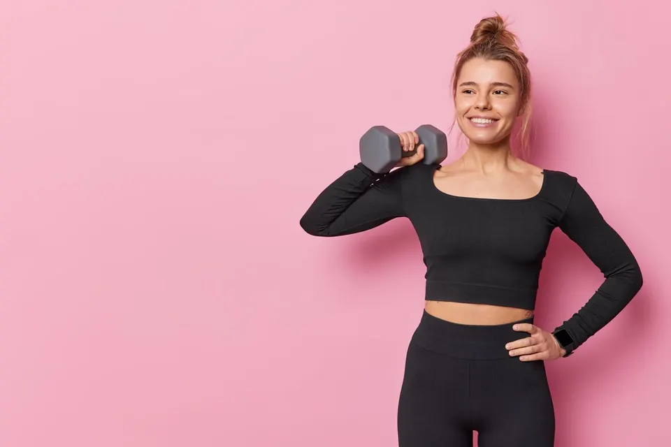 Mujer sonriente con una mancuerna sobre fondo rosa